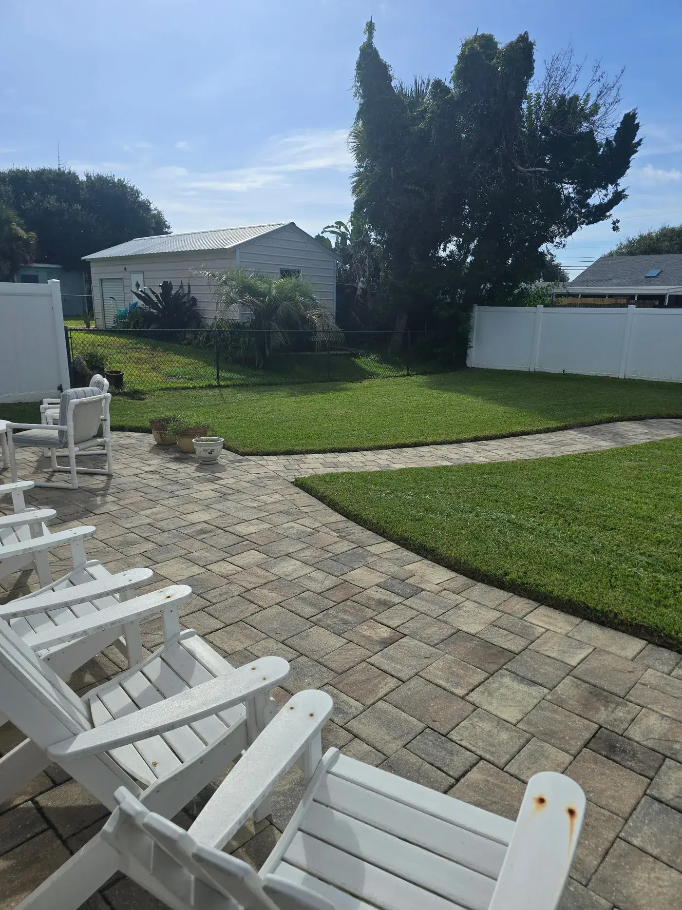 A residential patio and lawn with outdoor chairs and a curved paver walkway.