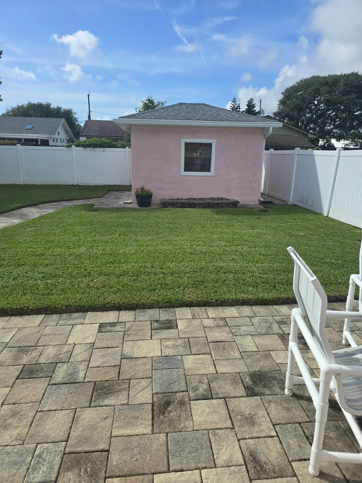 A tidy backyard lawn with a stone patio path and a small pink outbuilding.