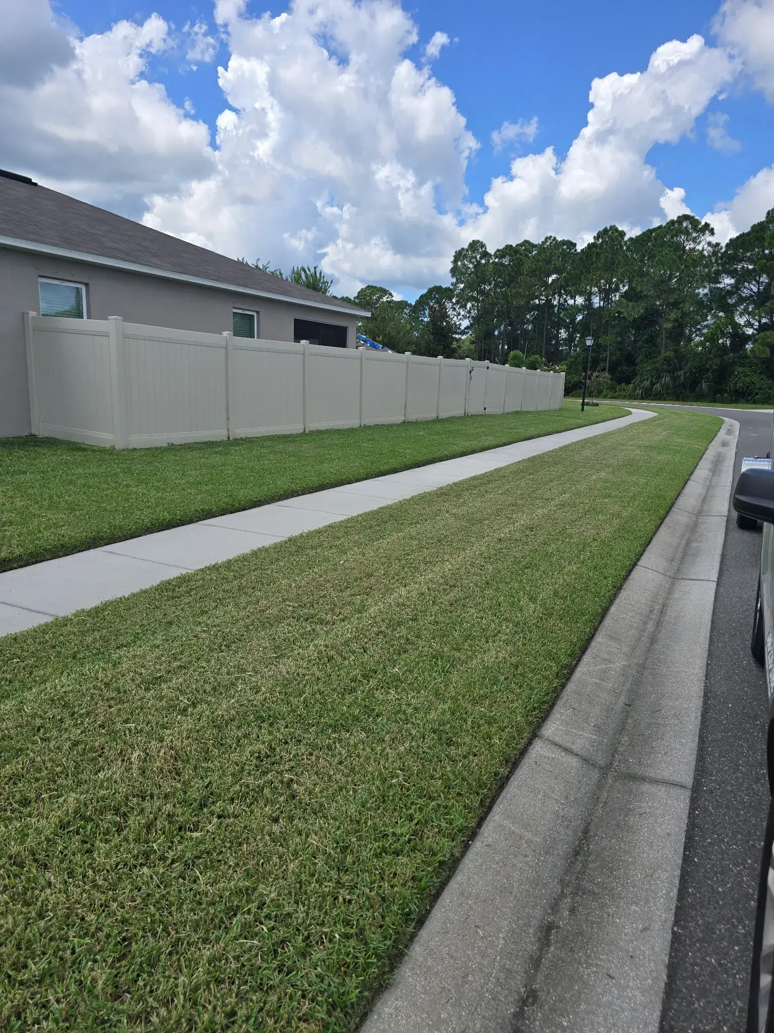 A freshly maintained residential lawn with clean edges along a long sidewalk and white fence.